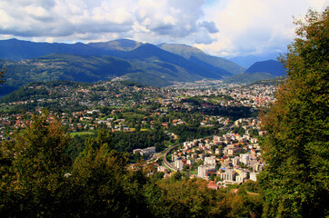 Fototapeta na wymiar Panoramic view of the mountains and a city at their feet from Mount San Salvatore in the city of Lugano, in southern Switzerland 