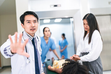 Portrait of young handsome Asian male doctor rushing in hospital during emergency with patient lying on bed with mother holding hand and nurse assisting in corridor passage