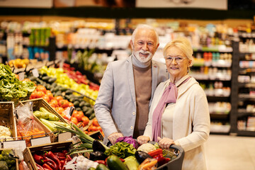 A happy healthy senior couple is buying fresh vegetables at the supermarket.
