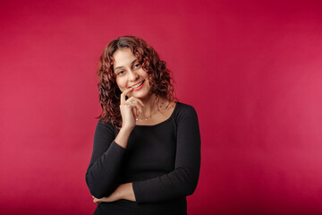 Fototapeta premium Young redhead girl smiling happy wearing black ribbed dress isolated over red background finger touch teeth ceramic wonder. Smiles at the camera with hope and joy.