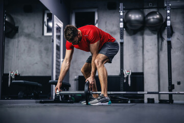 Fototapeta na wymiar A photo shoot of a handsome man in a red shirt and shorts setting up equipment for training in a modern sports center. Fitness challenge, cross-fit, weightlifting