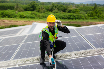 Handsome young male engineer wearing safety vest and jacket with gloves and tools along with hard hat helmet standing on solar panel while checking and looking at its maintenance