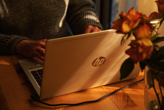 Paris, France - February 9, 2022: Man working from home at simple workplace with HP laptop computer in sunset light. Remote working from home in comfortable working environment.