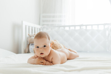 Caucasian little baby is lying on his stomach on a white sofa