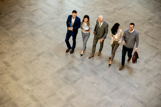 A Group Of Young And Senior Business People Are Walking In An Office Hallway, Captured In An Aerial View. They Are Dressed In Formal Attire