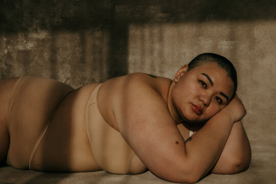 plus size filipino woman with shaved head lying on floor in the sun looking at camera