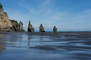 Strand mit schwarzem Sand und Felsen und Pfützen in Neuseeland bei den Three Sisters.