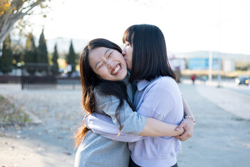 Naklejka premium Happy lifestyle of a young Asian couple playing with each other outside. The short-haired girl gives the long-haired woman a kiss on the face. Outdoor lifestyle concept.