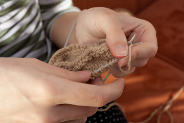 Obraz premium Female hands knitting with beige wool. Close-up of woman knits scarf, sweater, socks or mittens. Process of knitting