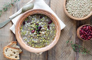 Bean soup in a ceramic bowl with a sprig of thyme on a wooden table. A mix of red beans, lentils and peas. The concept of vegetarian food. Rustic style. Horizontal orientation. Top view