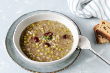 Bean soup in a ceramic gray bowl with a sprig of thyme and a piece of bread on a grey background. A mix of red beans, lentils and peas. The concept of vegetarian food. Horizontal orientation.