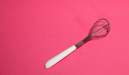 Manual metal whisk for whipping cream for baking desserts on a pink background. Baking concept.
