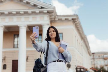 Fototapeta premium Portrait of thai student girl taking a self portrait with smart phone. Modern millennial youth lifestyle and travel concept.
