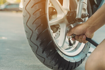 Hands of man check inflator pressure and inflates a tire on motorcycle with an air compressor. Man...