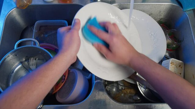 Top view of male hands washing dishes in the kitchen. Pile of dirty dishes hands washing in the kitchen sink in slow motion. Dishwashing procedure, plenum box. 