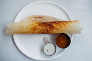 Dosa Ghee roast Dosa, famous south Indian breakfast item which is made in caste iron pan in traditional way and arranged on a white base with side dish ,on a white background