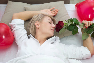 Cute modern girl lying on bed and smelling red roses.