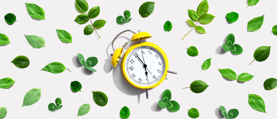 Yellow vintage alarm clock with green leaves - flat lay