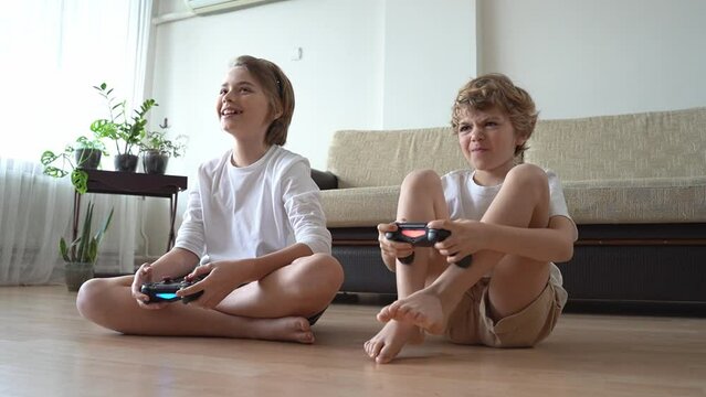 Funny caucasian siblings are relaxing together, playing video games in front of tv, two brother sister expressing emotions while enjoying their hobby playstation joystick