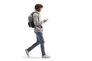 Full length profile shot of an african american male with a backpack walking and using a mobile phone - obrazy, fototapety, plakaty