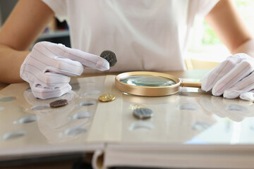 Fototapeta na wymiar Numismatist in white gloves examines ancient coins collection at table.