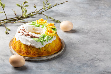 Easter cake decorated with icing and spring flowers with Easter eggs and willow twigs on gray background. Happy easter holiday.