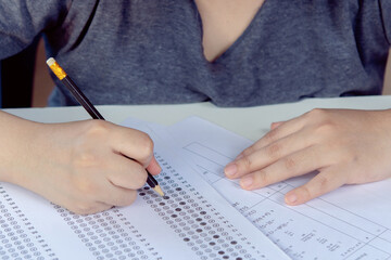 Students hand holding pencil writing selected choice on answer sheets and Mathematics question sheets. students testing doing examination. school exam