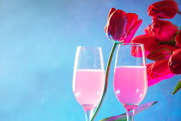 A bouquet of spring tulips and two glasses of pink champagne on a blue background . International Women's Day, copy space
