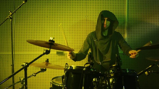 Drummer performs at percussion instruments at rock concert. Tympanist man plays drums, musical cymbals at show. Musician in hoody at rehearsal, participates in recording of album in sound studio