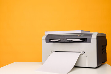 Front view of a light printer and a blank A4 paper on a white table on a yellow background, mockup.Office equipment, close-up.Copy space.Multifunction device. Multifunction printer.