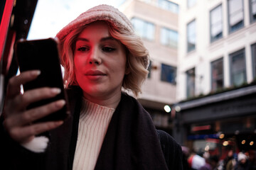 Young woman using phone standing beside red neon.