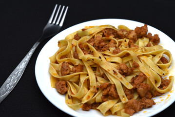 Italian pasta on a white plate with a fork. A plate of vermicelli with meat on a black background.