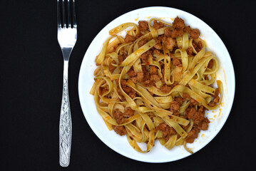 Italian pasta on a white plate with a fork. A plate of vermicelli with meat on a black background.