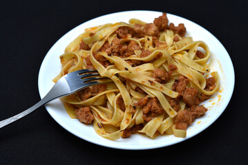 Italian pasta on a white plate with a fork. A plate of vermicelli with meat on a black background.