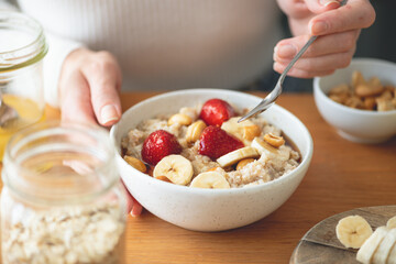 Woman eating oatmeal porridge with banana strawberry and cashew nuts. Healthy vegetarian breakfast food - 569307139