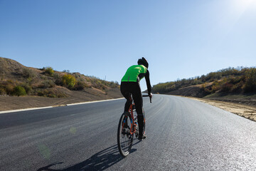 Fototapeta premium Cyclist riding bicycle on road against clear sky