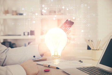 Double exposure of man's hands holding and using a digital device and bulb hologram drawing. Idea concept.