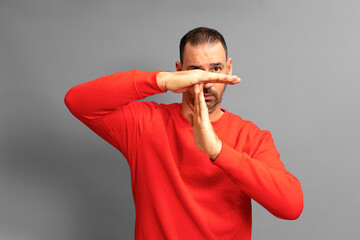 Studio shot of serious man in red jumper making time out gesture need to stop and asking for time to rest after hard work showing broken hand sign. Isolated from gray background body language concept.