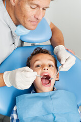  dentist examining teeth of boy. dentist in gloves using tooth on teeth of little patient while cute boy looking at camera during checkup procedure