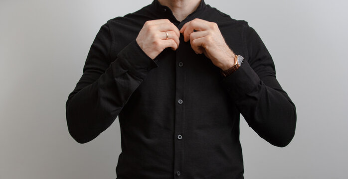 Unrecognizable man in black shirt fasten button at grey background