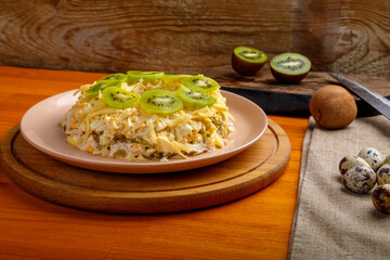 Salad with chicken and kiwi on a stand next to quail eggs on a kiwi napkin on a board and a knife on the table.