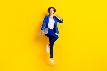 Fototapeta na wymiar Full length photo of positive confident lady dressed blue blazer jumping thumb up holding gadget isolated yellow color background