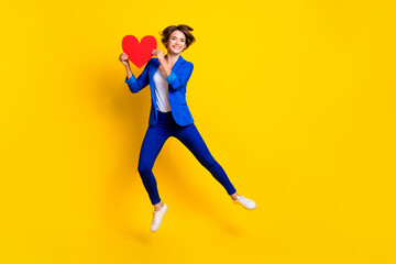 Fototapeta na wymiar Full length photo of charming cute lady dressed blue blazer jumping high holding heart empty space isolated yellow color background