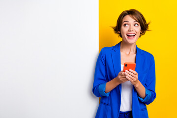 Photo of funny excited lady dressed blue blazer typing device looking white wall placard empty...