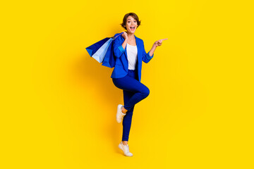 Fototapeta na wymiar Full length photo of excited funny lady dressed blue blazer holding bargains showing empty space isolated yellow color background