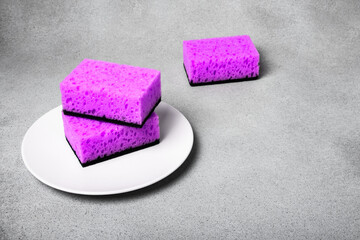 Lilac sponges for dishwashing on a white plate on a neutral gray background. Gentle dishwashing. House cleaning.