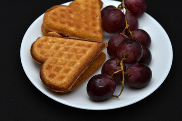Delicious waffles and grapes on a plate. A sweet breakfast of waffles and red grapes. Heart-shaped waffles.