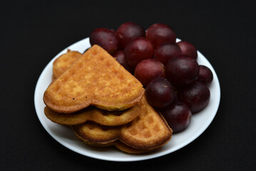 Delicious waffles and grapes on a plate. A sweet breakfast of waffles and red grapes. Heart-shaped waffles.