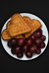 Delicious waffles and grapes on a plate. A sweet breakfast of waffles and red grapes. Heart-shaped waffles.