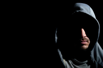 Horizontal portrait shot of mysterious young bearded hooded man with his face covered in shadows...